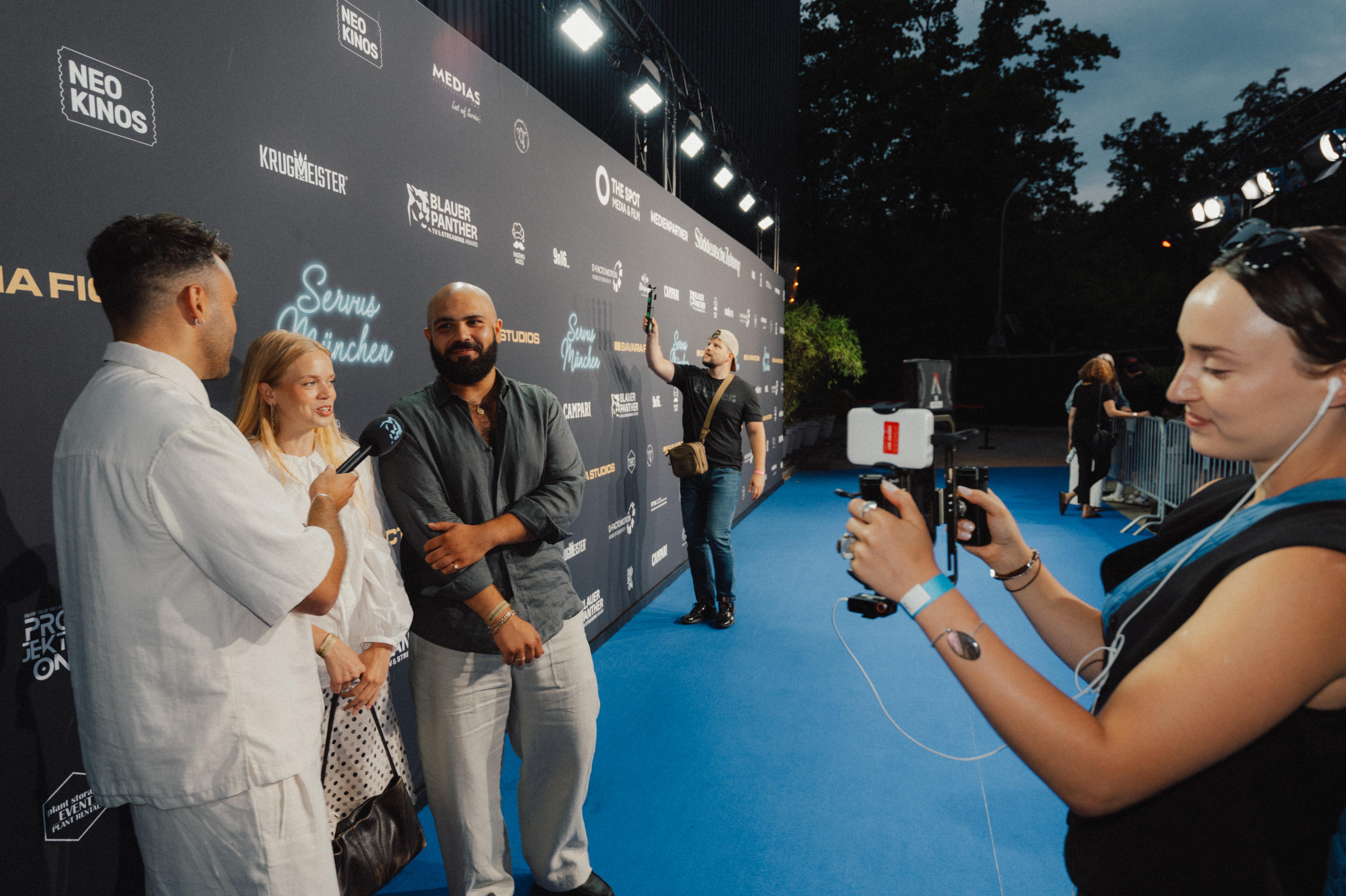 Blauer Teppich der Servus München Party, ein Interview vor der Sponsorenwand