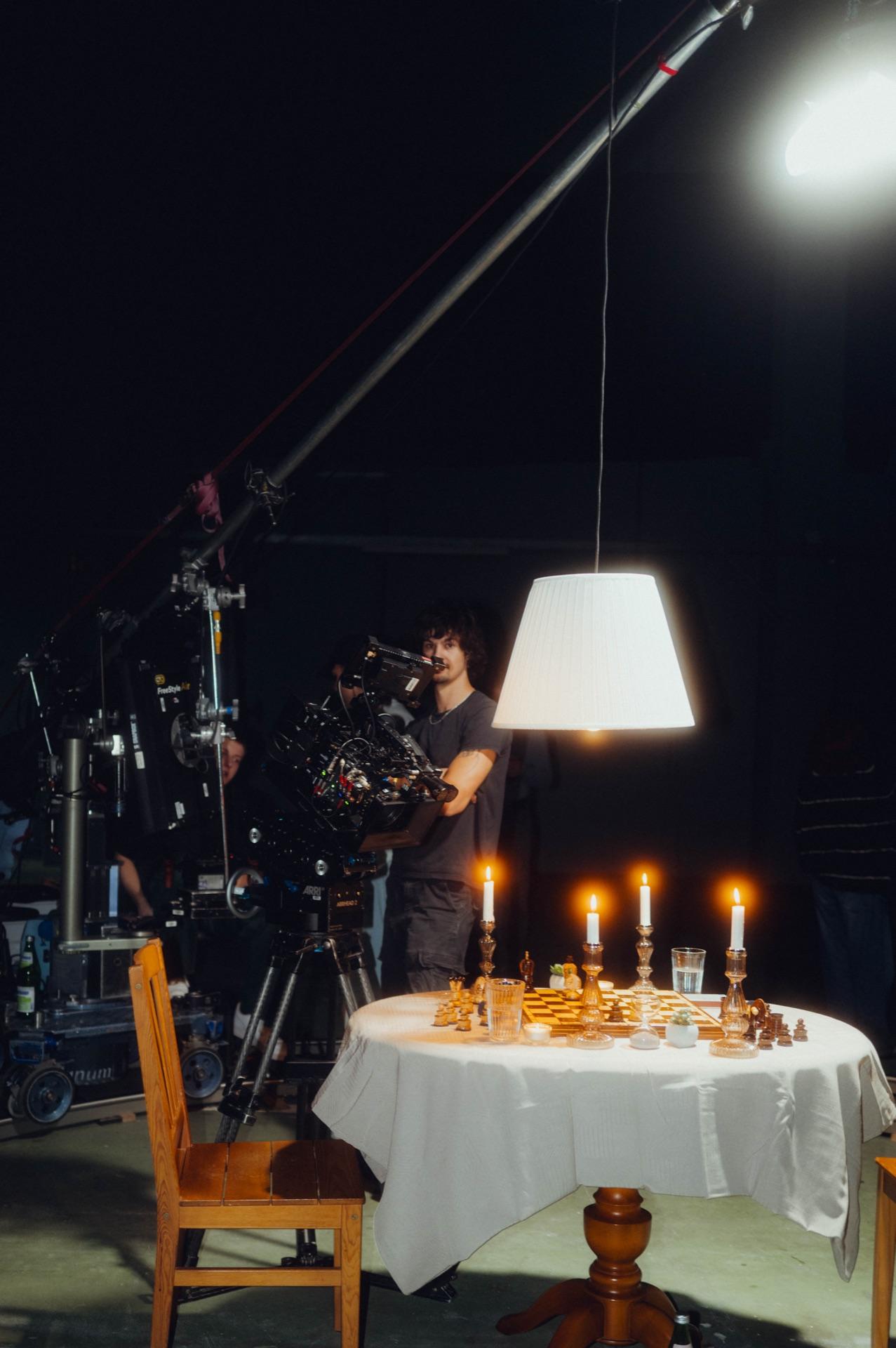 Das Set: der gedeckte Tisch mit Schachbrett und Kerzen unter einer Hängelampe, Kamera davor