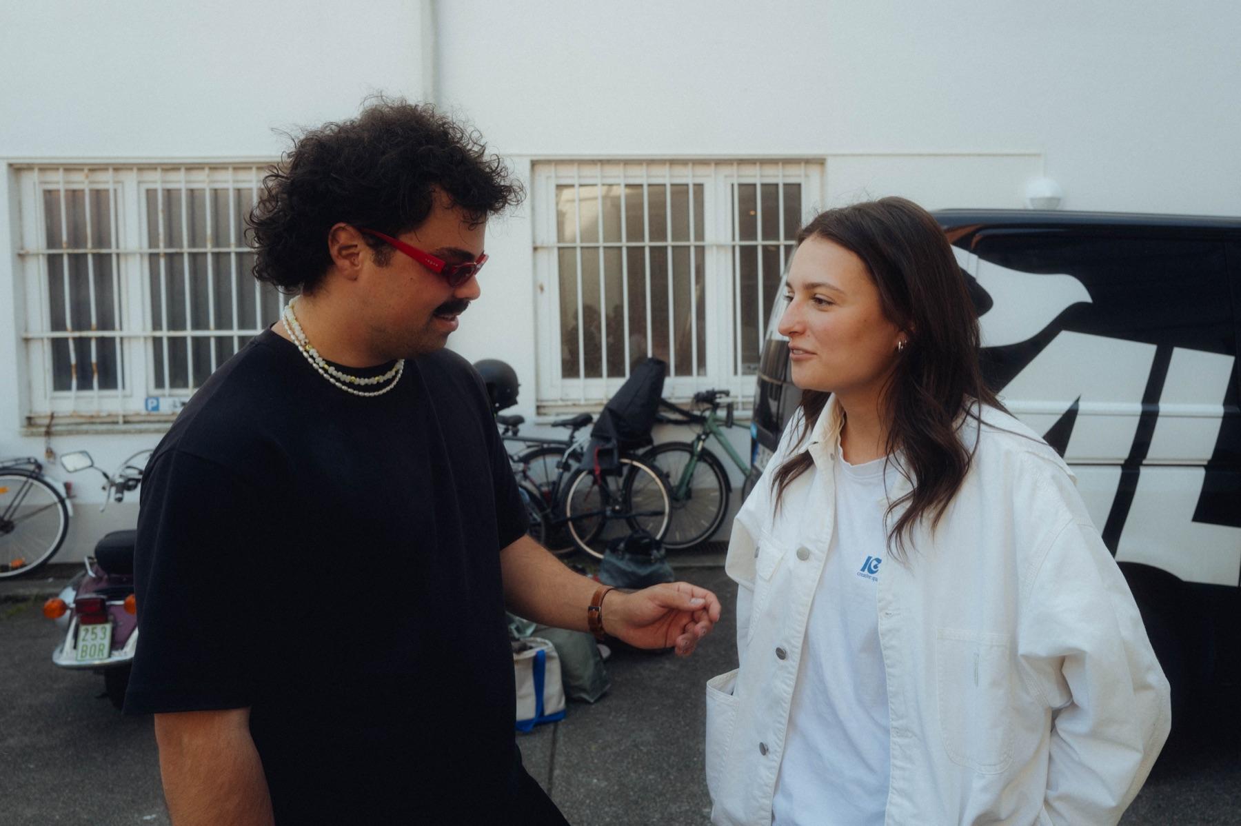 Behind the Scenes: zwei Crew-Mitglieder im Gespräch im warmen Abendlicht, ein Mann mit roter Brille und eine Frau in heller Jacke