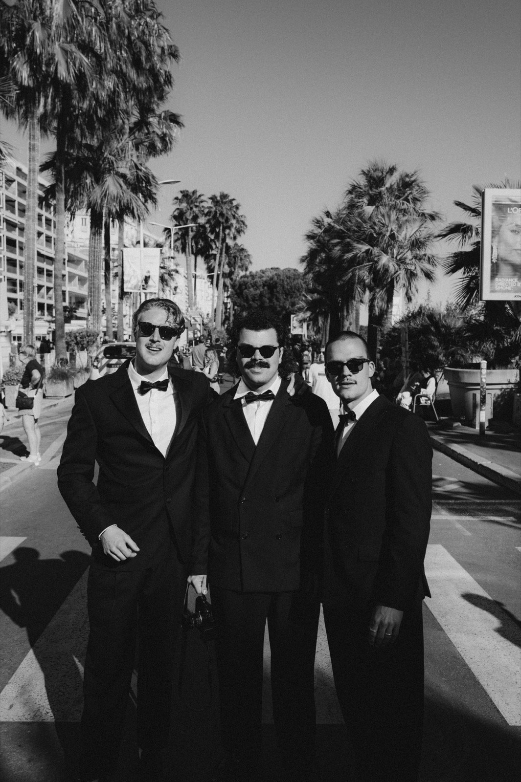 Jakob Hermann Hähner, Lino Kalkhoff und Johannes Fielers im Smoking vor Palmen an der Croisette, schwarzweiß