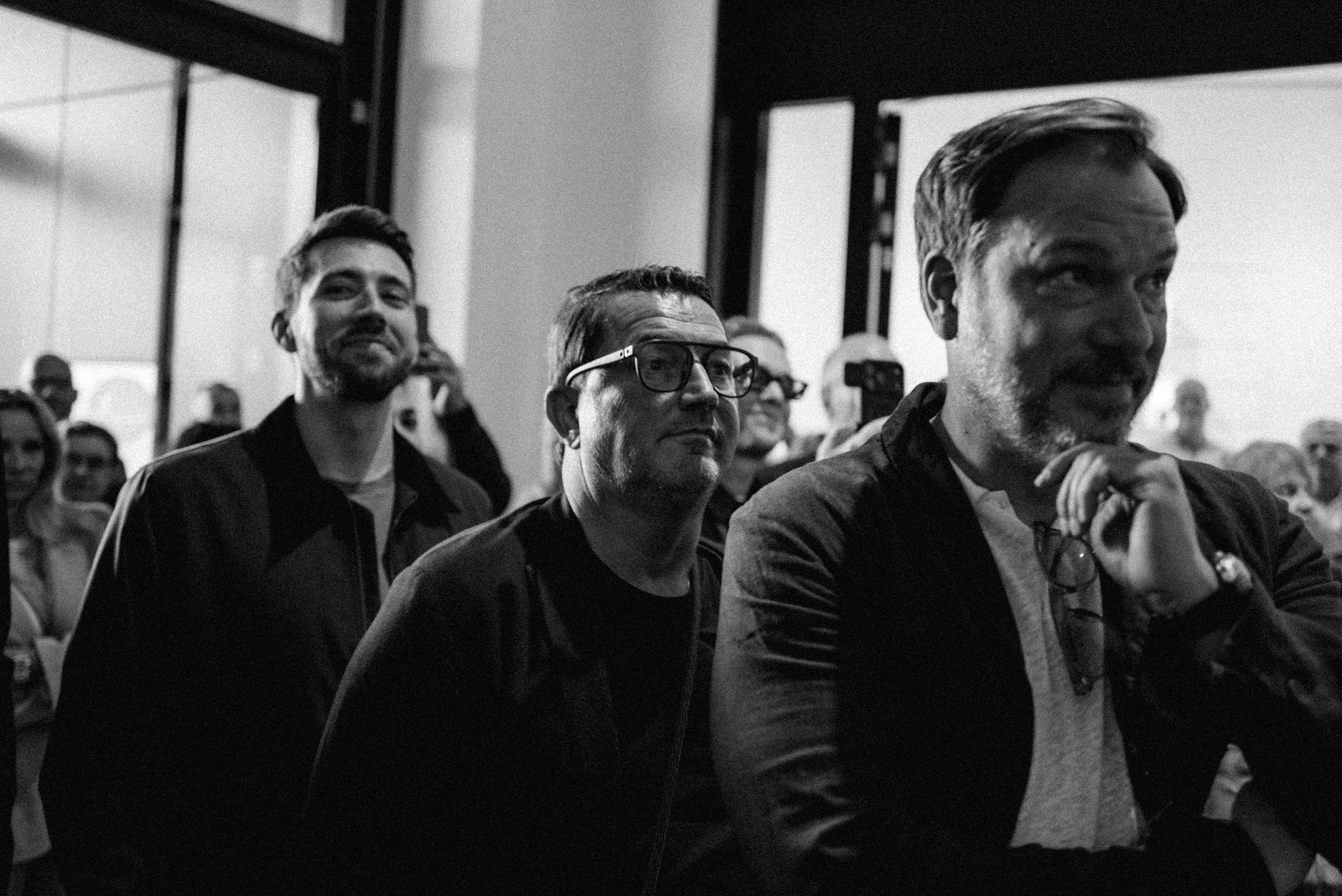 Drei Gäste der Vernissage schauen konzentriert in dieselbe Richtung, schwarzweiß