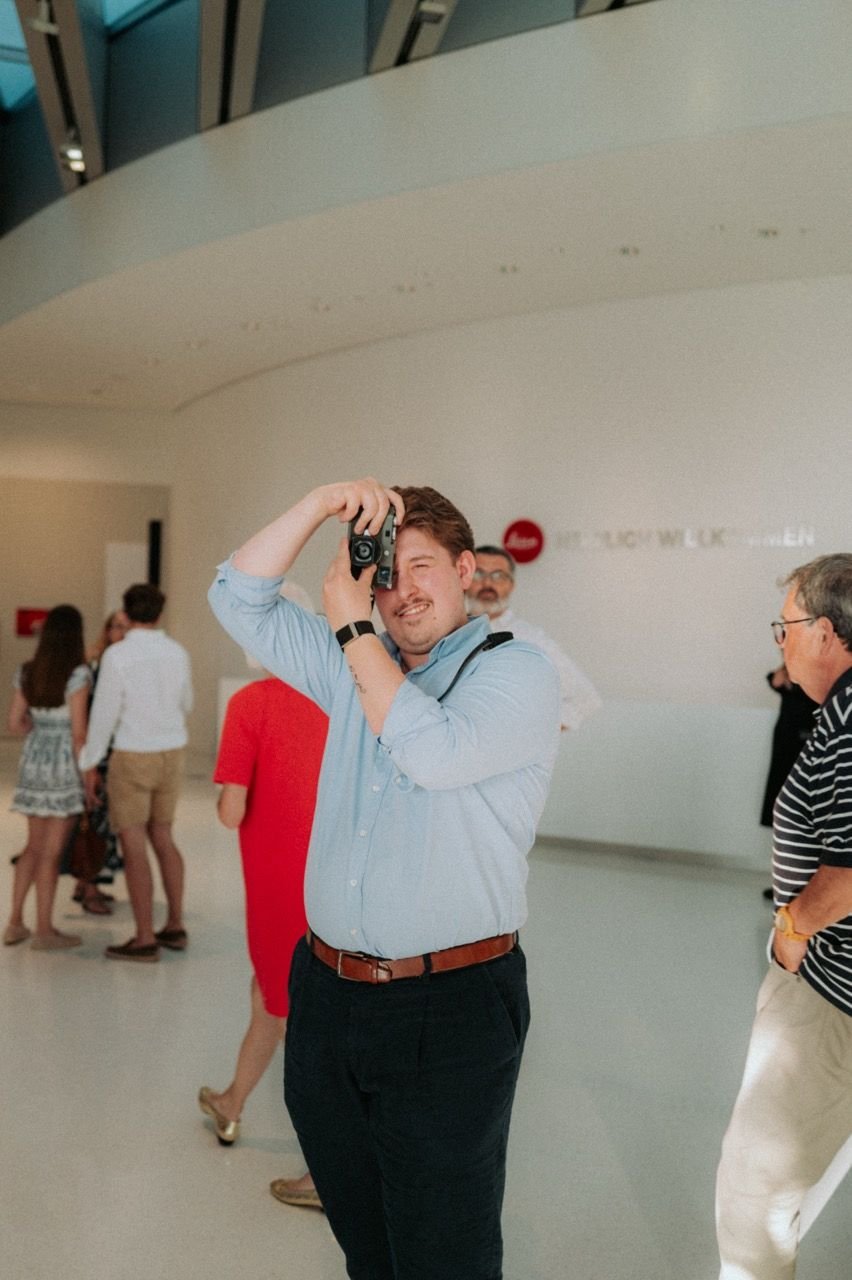 Person hebt eine Leica-Kamera vor das Auge und fotografiert im Rundgang der Galerie