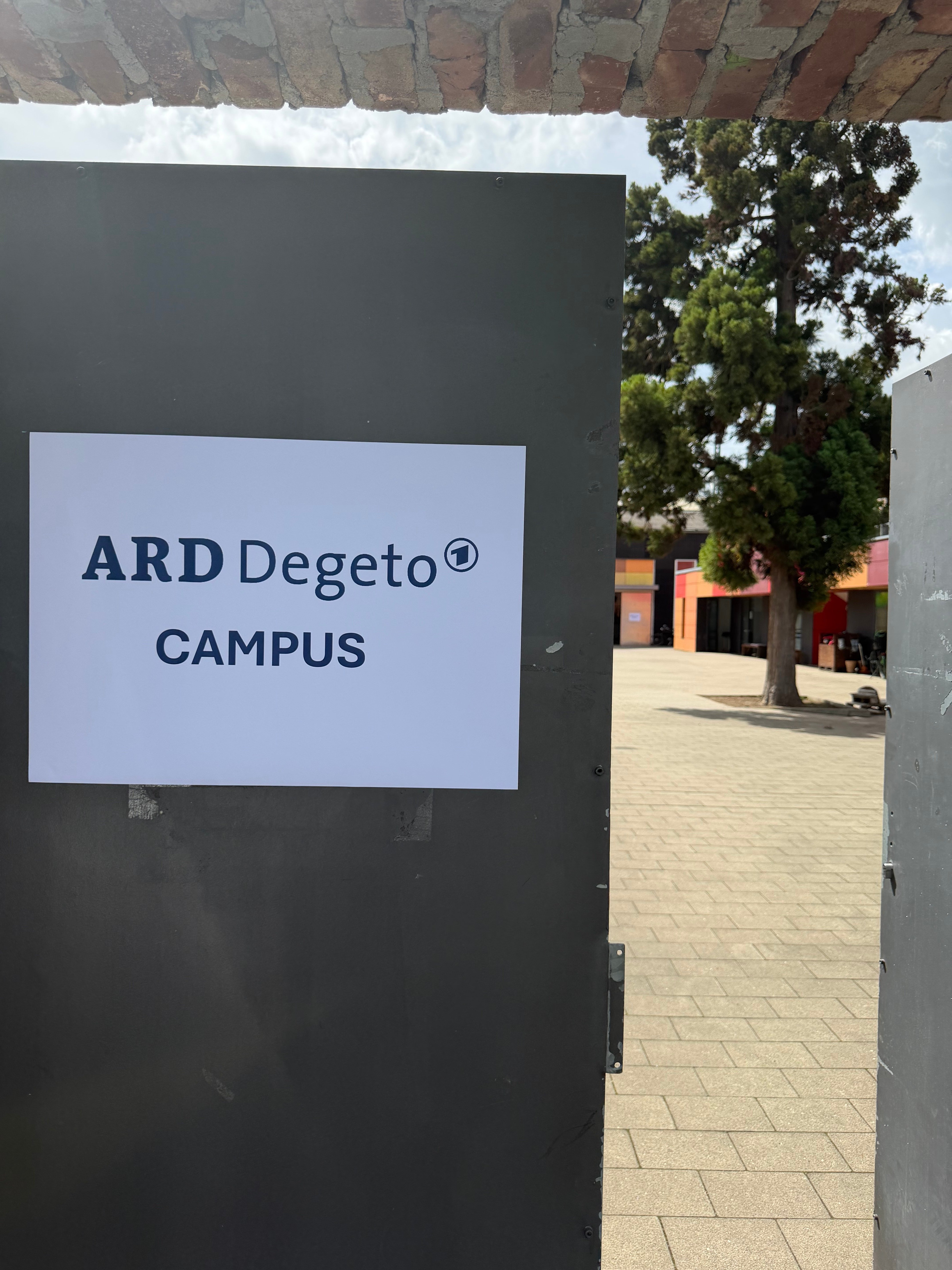 Schild „ARD Degeto Campus“ an einer dunklen Tafel zwischen Backsteinmauern
