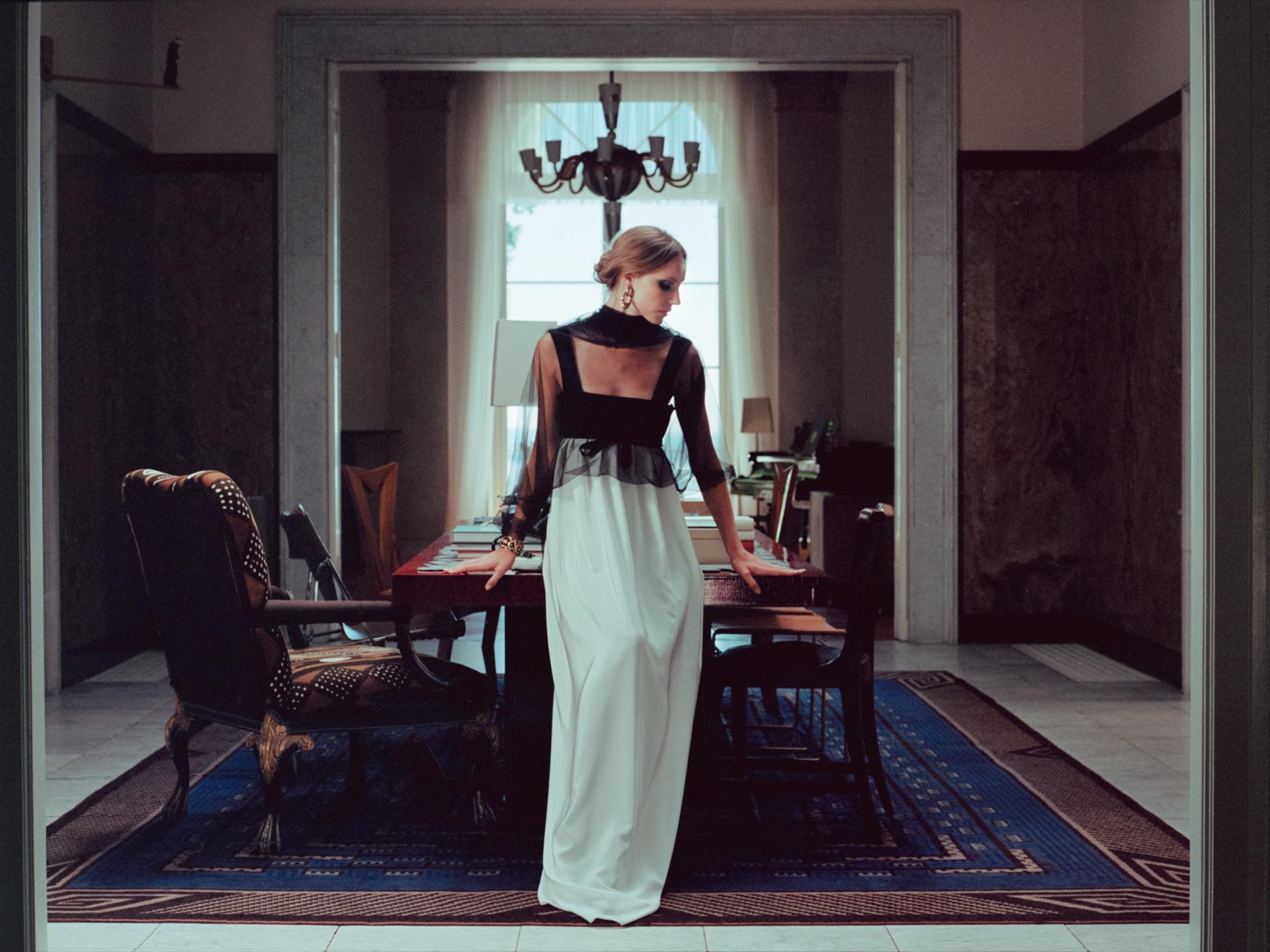Modell in heller Robe in einem Speisesaal unter einem Kronleuchter