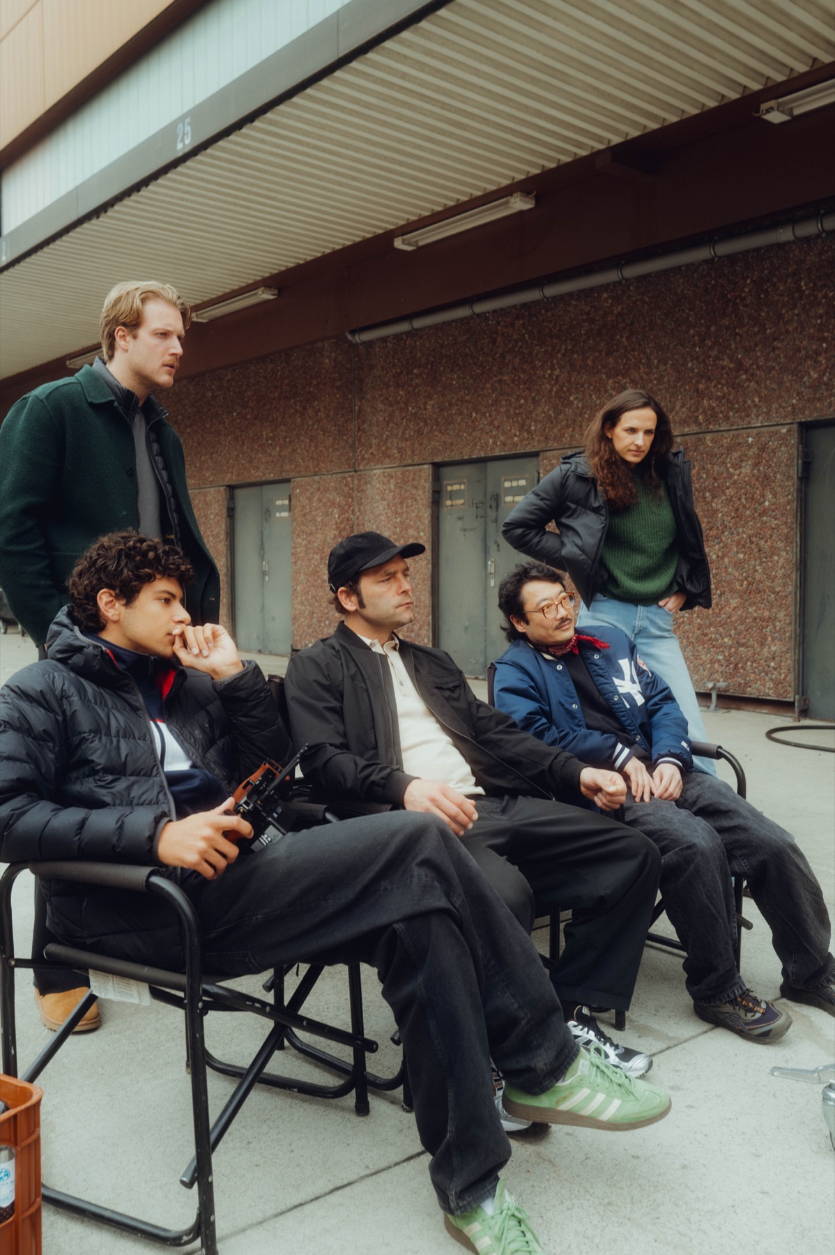Crew und Cast warten auf Regiestühlen am Set